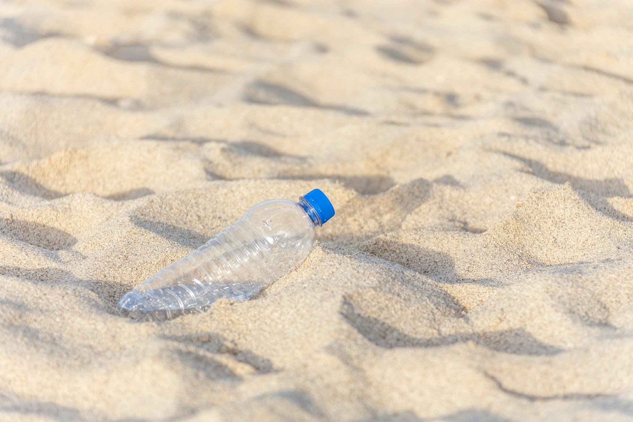Discarded plastic bottle on sand, illustrating beach pollution problem.
