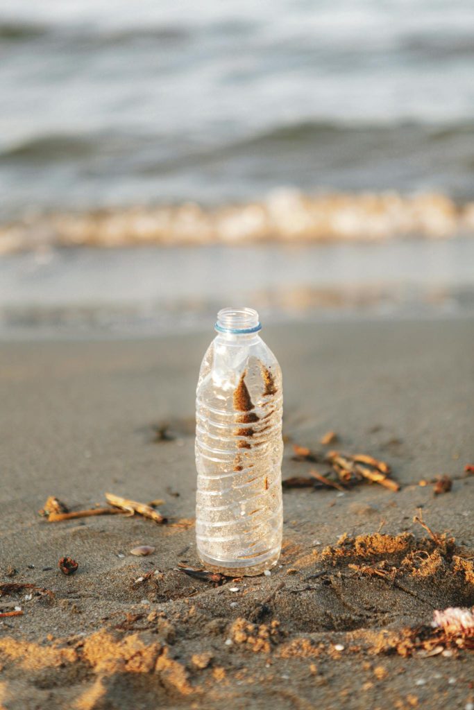Plastic bottle on sandy shore highlights pollution issue.